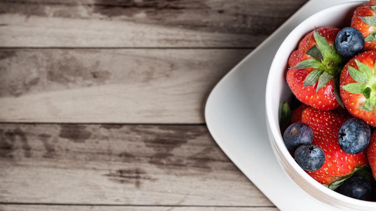 Vibrant strawberries and blueberries in a white bowl on a wooden table. Perfect for food photography.